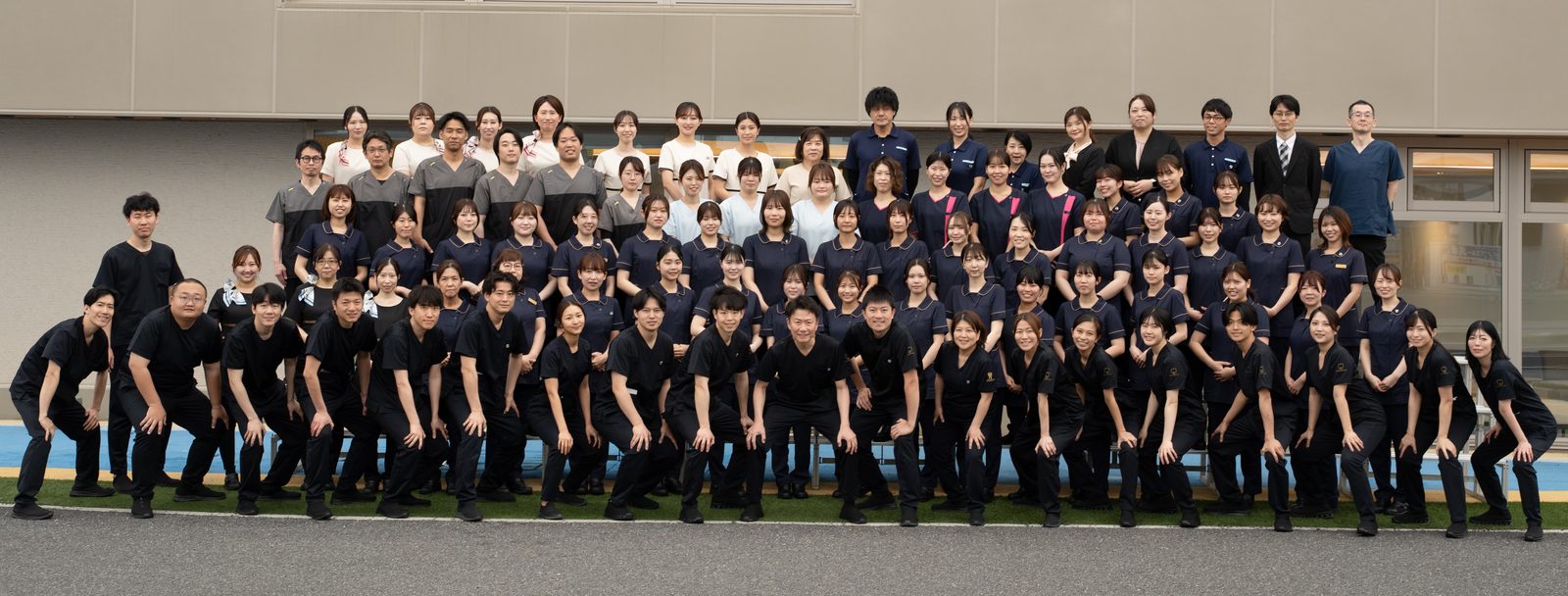 やまむら総合歯科・矯正歯科のスタッフ一同が医院の前に並び、応援のポーズをとっている集合写真